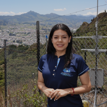 Retrato de Jessica Katherine Gaona Alvarado con el uniforme del Grupo de Investigación en Hidroinformática, frente a una estación de monitoreo ambiental con vista panorámica de Loja.